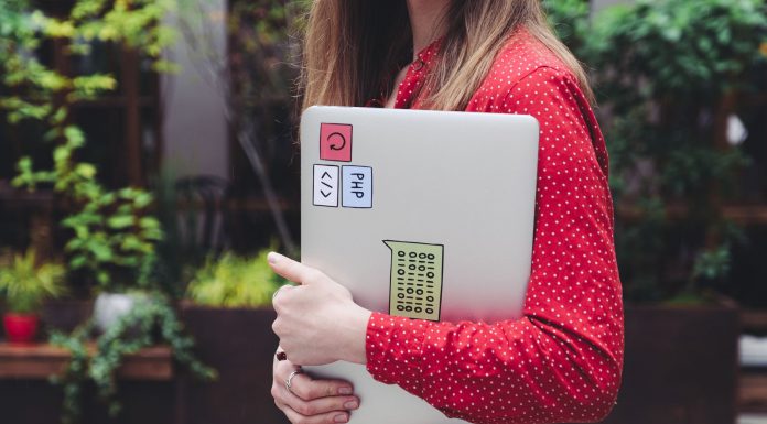 ÚLTIMA HORA: Hopeworks abre centro de desarrollo laboral en Newark A young woman in a red polka dot shirt holds a laptop with stickers outdoors.