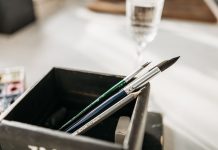 Detailed image of paintbrushes and pencil in a holder with soft light.