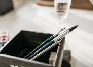 Detailed image of paintbrushes and pencil in a holder with soft light.