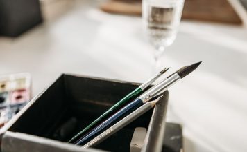 Detailed image of paintbrushes and pencil in a holder with soft light.