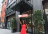Woman in red dress holds 'SOLD' sign outside office building, symbolizing real estate success.