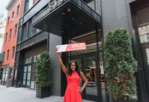 Woman in red dress holds 'SOLD' sign outside office building, symbolizing real estate success.