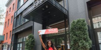 Woman in red dress holds 'SOLD' sign outside office building, symbolizing real estate success.