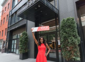 Woman in red dress holds 'SOLD' sign outside office building, symbolizing real estate success.