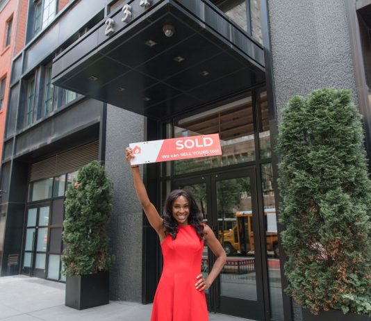 Woman in red dress holds 'SOLD' sign outside office building, symbolizing real estate success.