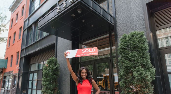 ÚLTIMA HORA: Propiedad en Westfield se vende por $3.7 millones para reurbanización Woman in red dress holds 'SOLD' sign outside office building, symbolizing real estate success.