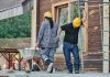 Two construction workers wearing hard hats work at an outdoor site, one with a wheelbarrow.