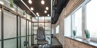 Black leather pedicure chair placed between glass door and window in modern beauty salon with decorated plants and glowing lamps