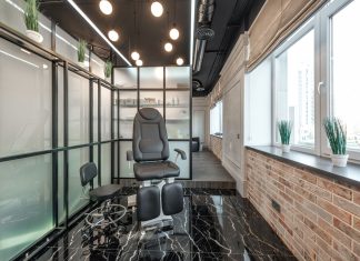 Black leather pedicure chair placed between glass door and window in modern beauty salon with decorated plants and glowing lamps