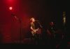 Live rock band performing on stage with vibrant red lighting creating a dynamic atmosphere.