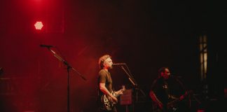 Live rock band performing on stage with vibrant red lighting creating a dynamic atmosphere.
