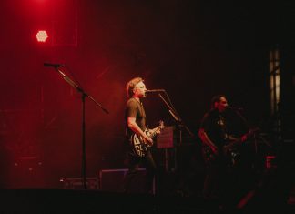 Live rock band performing on stage with vibrant red lighting creating a dynamic atmosphere.