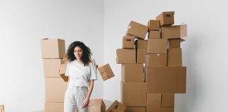 Young female with curly hair between piles and flying cardboard containers after moving into house on light background