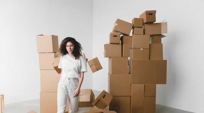 Young female with curly hair between piles and flying cardboard containers after moving into house on light background