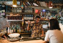 Bartender mixing a cocktail for a customer in a trendy urban bar with extensive liquor collection.