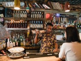 Bartender mixing a cocktail for a customer in a trendy urban bar with extensive liquor collection.