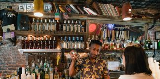 Los Mejores Bares en West New York para 2026: Tu Guía Definitiva de Vida Nocturna Bartender mixing a cocktail for a customer in a trendy urban bar with extensive liquor collection.