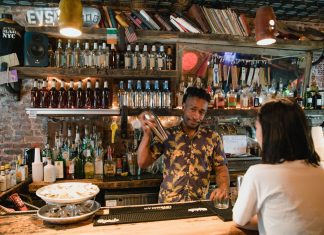Bartender mixing a cocktail for a customer in a trendy urban bar with extensive liquor collection.