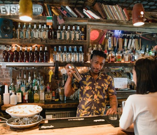 Bartender mixing a cocktail for a customer in a trendy urban bar with extensive liquor collection.