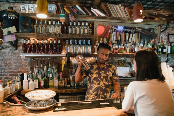 Bartender mixing a cocktail for a customer in a trendy urban bar with extensive liquor collection.
