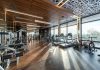 Modern exercise bikes and treadmills and various fitness equipment in spacious gym with wooden floor and panoramic windows in sunlight