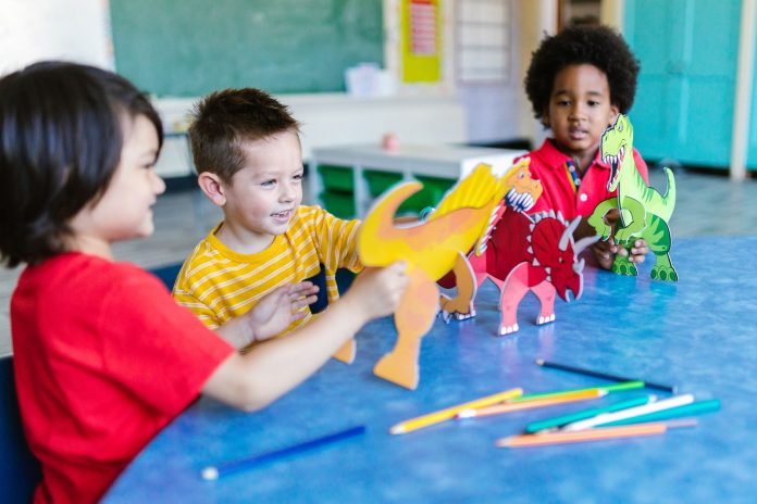 mejores-jardines-infancia-hoboken-guia-2026 Three kids playing with dinosaur figures, fostering imagination and learning.