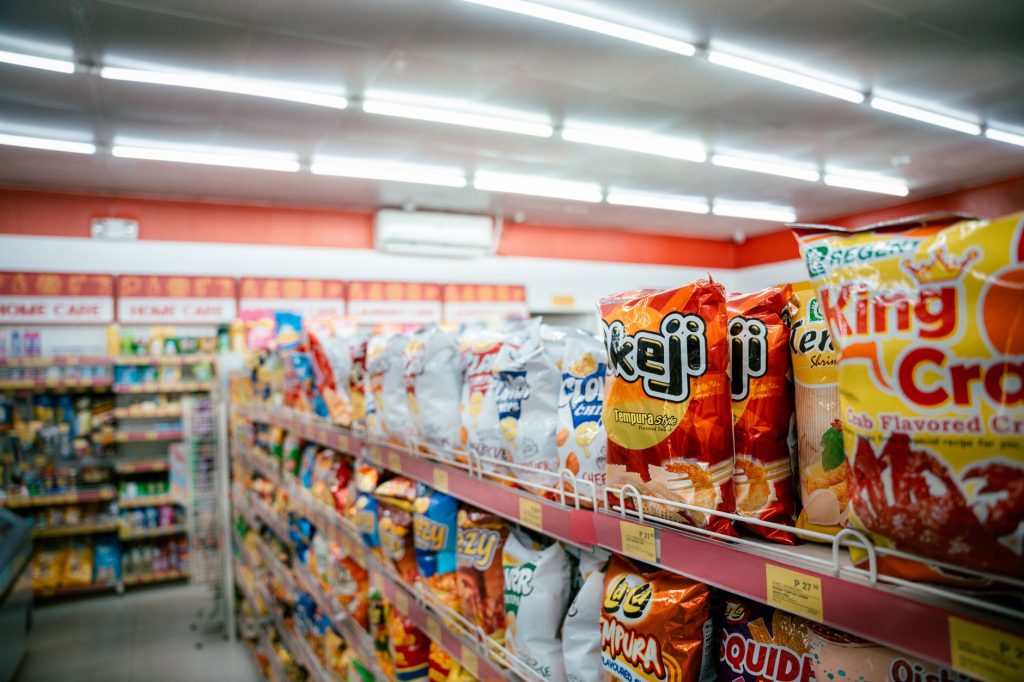Wide shot of vibrant snack aisle in a supermarket with various chip bags on display.