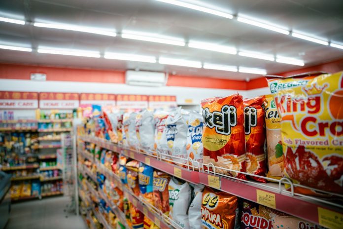 Wide shot of vibrant snack aisle in a supermarket with various chip bags on display.