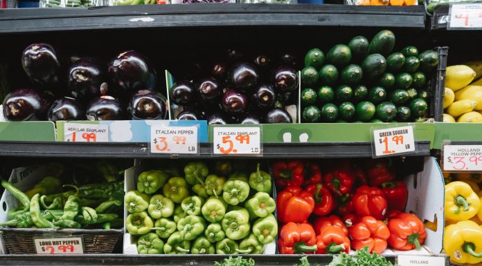 Colorful assortment of vegetables on display in a supermarket, featuring peppers, eggplants, and squash.