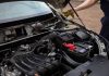 Mechanic inspecting car engine bay and battery during routine maintenance.