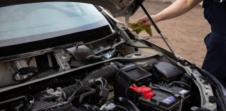 Mechanic inspecting car engine bay and battery during routine maintenance.