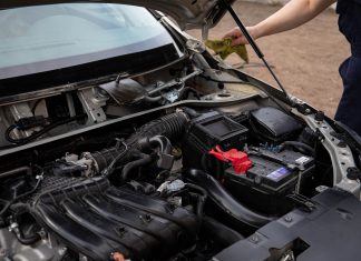 Mechanic inspecting car engine bay and battery during routine maintenance.