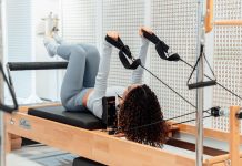 PETALED Blooms: New Pilates Studio Finds Home in Jersey City Heights A woman wearing a gray tracksuit exercises on a Pilates reformer in a modern studio setting.