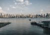 Panoramic view of New York City skyline from waterfront with a tranquil river foreground.