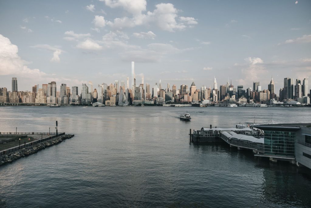 Panoramic view of New York City skyline from waterfront with a tranquil river foreground.