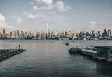 Panoramic view of New York City skyline from waterfront with a tranquil river foreground.