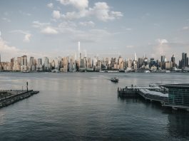 Panoramic view of New York City skyline from waterfront with a tranquil river foreground.