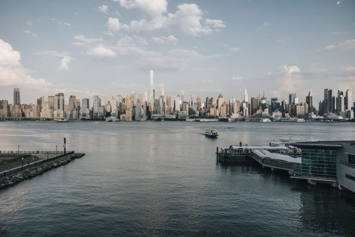 Panoramic view of New York City skyline from waterfront with a tranquil river foreground.