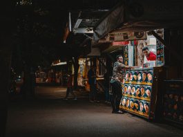 A vibrant night scene capturing an interaction at a street food stall with illuminated menus.