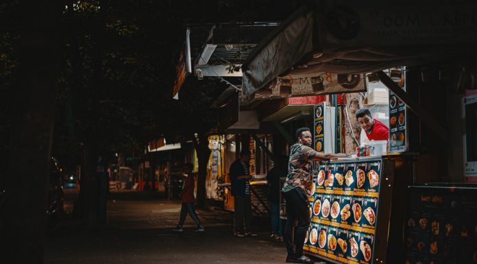 A vibrant night scene capturing an interaction at a street food stall with illuminated menus.