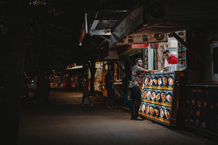 A vibrant night scene capturing an interaction at a street food stall with illuminated menus.