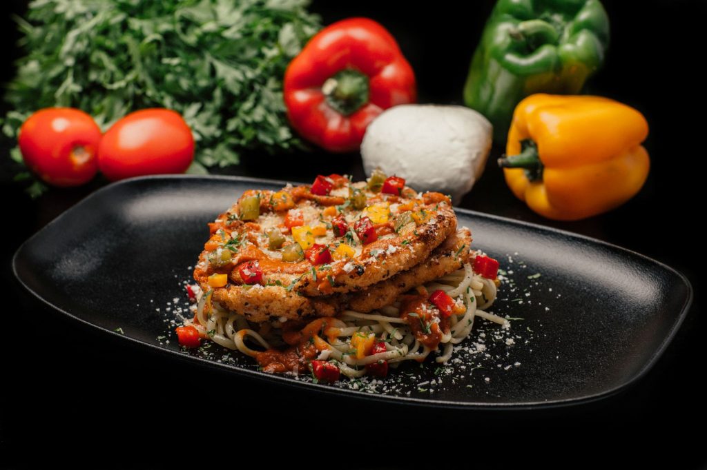 Savor a mouthwatering dish of chicken pasta garnished with fresh vegetables on a stylish black plate.