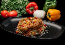 Savor a mouthwatering dish of chicken pasta garnished with fresh vegetables on a stylish black plate.