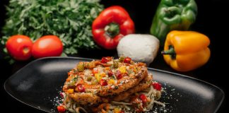 Savor a mouthwatering dish of chicken pasta garnished with fresh vegetables on a stylish black plate.