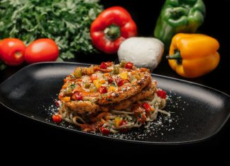 Savor a mouthwatering dish of chicken pasta garnished with fresh vegetables on a stylish black plate.