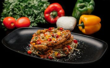 Savor a mouthwatering dish of chicken pasta garnished with fresh vegetables on a stylish black plate.