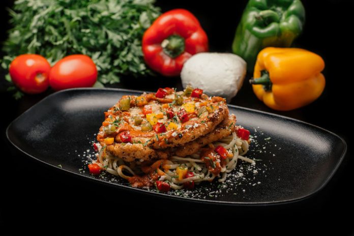 Savor a mouthwatering dish of chicken pasta garnished with fresh vegetables on a stylish black plate.