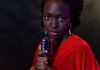 Elegant woman in red with vintage microphone against dark background, conveying emotion.