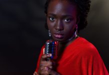 Elegant woman in red with vintage microphone against dark background, conveying emotion.