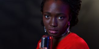 Elegant woman in red with vintage microphone against dark background, conveying emotion.